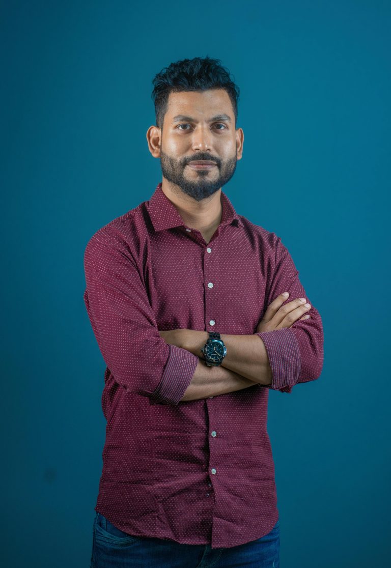 A confident man in a casual red shirt poses against a turquoise background, embodying modern style.